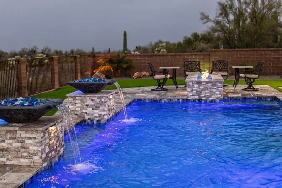 A luxury backyard in Tucson with a custom swimming pool, elegant hardscape, layered desert landscaping, accent lighting, and a cohesive resort-style design that visually connects the pool, patio, and planting.